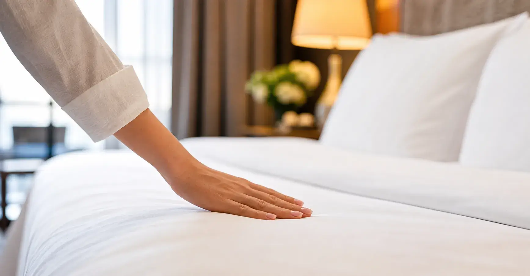 Guest touching crisp white hotel bedding in luxury room